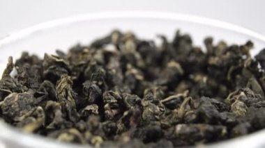 Beyaz arka planda cam bardakta pişmemiş kuru yeşil çay barutu. Döndürme