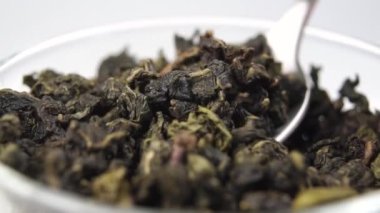 Çay kaşığının içinde kurumuş yeşil çay yaprakları. Ağır çekimde bir fincan tam pişmemiş çaya düşür.
