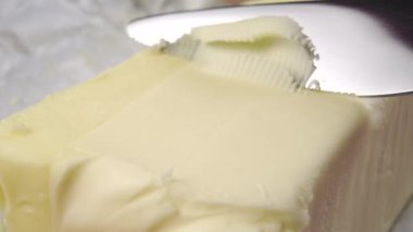 Mutfak bıçağı bir parça tereyağını yakın plan çekimle keser. Güzel yağlı ince talaşlar. Makro çekim