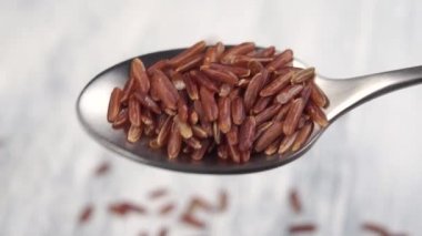 Esmer pirinç ağır çekimde metal kaşıktan düşer. Makro atış. Uzun buğday. Yakın çekim.