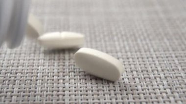 Beyaz tıbbi tedavi hapları plastik bir kaptan plastik bir paspasın üzerine yavaş çekimde düşer. Makro çekim