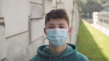 Güneşli bir günde üniversite binasının arka planında tıbbi maske takmış neşeli bir öğrenci. Okul konseptine dönelim.
