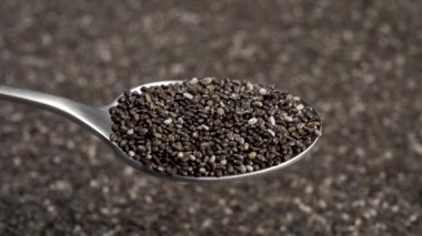 Metal kaşık dolusu chia tohumu yakın plan. Makro. Arkaplan tahıl yığınını bulanık olarak döndürür