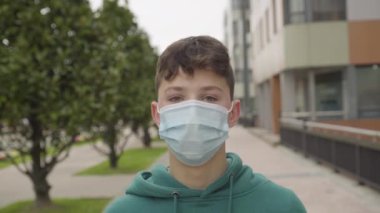 Şehir caddesinde tıbbi koruyucu maske takan genç bir öğrencinin şaşkınlığı ve şoku. Yakın plan portre. Pozitif ifade WOW