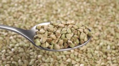Tam bir metal kaşık pişmemiş yeşil karabuğday taneleri dönen bir tohum yığınının arka planına karşı. Makro çekim