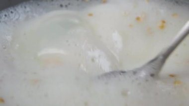 Sütlü ve yulaf ezmeli hazır lapa. Metal kaşık mısır gevreğiyle süt ürünlerini yavaş çekimde karıştırır. Makro çekim