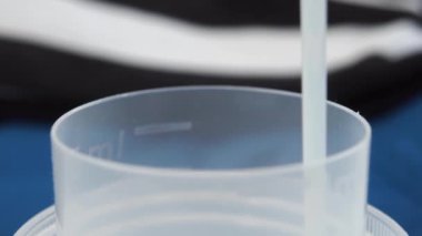 Çamaşırhanenin arka planına karşı plastik bir ölçü kepine beyaz sıvı deterjan dökülüyor. Ağır çekim. Makro atış. Ev işleri konsepti