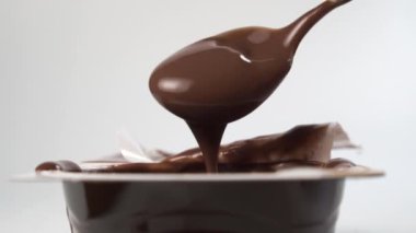Çikolatalı kremalı krema çay kaşığından plastik bardağa yavaş çekimde akıyor. Tatlı kalın kakaolu tatlı.