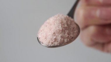 Bir çay kaşığı dolusu Himalaya pembe tuzu. Hafif arkaplanda yavaş çekimde düşen baharat kristalleri