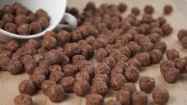 Çikolatalı gevrek taneleri yavaş çekimde mutfak tahtasına devrilmiş beyaz bir bardakla düşer. Lezzetli tatlı sabah topları. Makro çekim