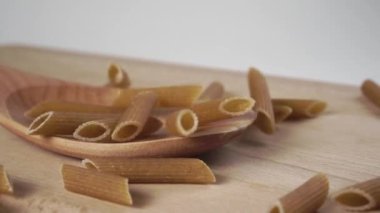 Bütün çiğ ekolojik makarna ağır çekimde tahta kaşık ve kesme tahtasına düşüyor. Makro. Doli Vuruşu
