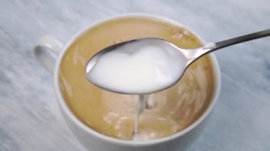 Soğuk süt çay kaşığına sıçrar ve sıcak espresso kahve bardağına dökülür. Ahşap dokuma sehpasında. Ağır çekim. Yakın plan.