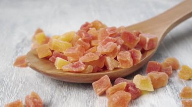 Kurutulmuş papaya dilimleri ahşap bir kaşığı dokulu bir yüzeyde ağır çekimde doldurur. Makro atış. Tatlı tropikal meyve