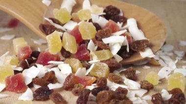 Tropikal meyve aperatiflerinin kuru dilimleri tahta kaşıktan yavaş çekimde tahtaya düşer. Makro atış. Hızlı vitamin karışımı. Papaya hindistan cevizi ananaslı kuru üzüm malzemeleri.