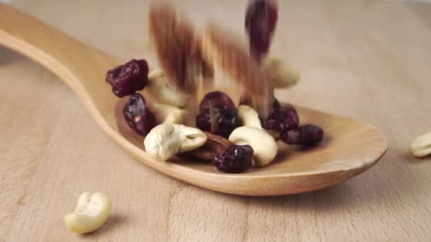ナッツフルーツミックスの成分は ボード上の木製のスプーンを埋めます 遅い動きで豆 カシューナッツ レーズンを落下させます 接近中だ ビタミンタンパク質スナック — ストック動画