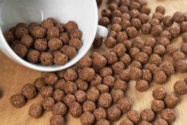 Çikolatalı gevrek topları beyaz bir fincanla tahtaya saçılmış. Yuvarlak pullar. Yakın plan.