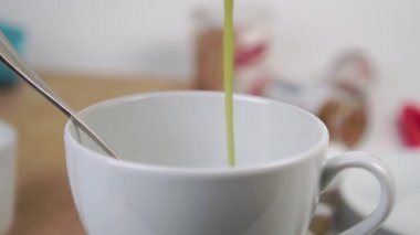 Yavaş çekimde beyaz bir çay fincanına sıcak yeşil kibrit çayı döküyorum. Yakın plan. Mutfak aletleri bulanık bir şekilde masanın üzerinde. Geleneksel Japon içeceği