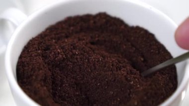 Beyaz bir fincanda öğütülmemiş kahve karışımı. Yavaş çekimde çay kaşığıyla karıştırmak. Makro atış. Aromatik geleneksel enerji doğal içeceği