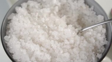 Gri bir kasede kaba deniz tuzu kristalleri. Yavaş çekimde kaşıkla karıştırmak. Makro çekim