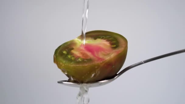 清澈的水流过半个褐色的番茄酱和慢动作的水花 在白色背景上的金属勺子上宏观射击 烹调前清洗蔬菜 — 图库视频影像