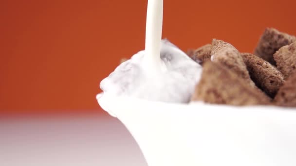 Молоко Наливають Білу Миску Шоколадними Крупами Яскраво Помаранчевому Тлі Розщеплюється — стокове відео