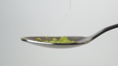 Yeşil kibrit çay tozu yavaş çekimde beyaz arka planda çay kaşığına düşer. Makro atış. Geleneksel Japon içeceği