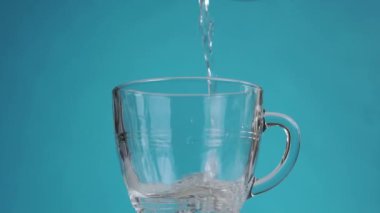 Temiz su, şeffaf bir bardağa yavaş çekimde akıyor. Renkli mavi bir arka planda. Saflık kavramı