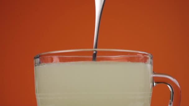 用溶解的泡腾片治疗药物饮料 慢动作时 用勺子在杯子里搅拌 在明亮的橙色梯形背景上 靠近点 — 图库视频影像