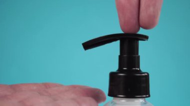 Ellerin hijyenik antibakteriyel temizliği için Coronavirus dezenfektanı jeli plastik bir kaptan parmaklarına dökülür. Renkli mavi bir arkaplanda.