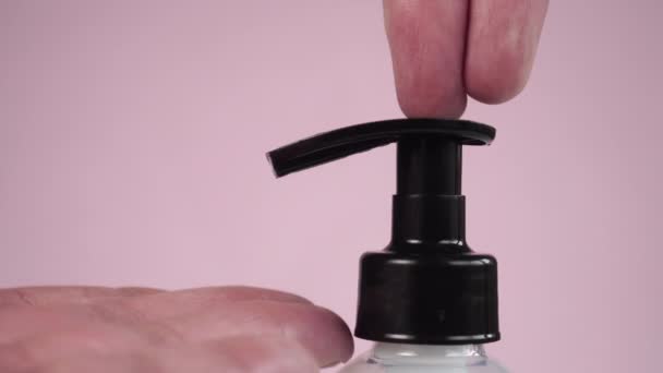 プラスチック製の容器から液体石鹸を使用して手を洗って消毒し 細菌やウイルスから保護します 衛生的なゲルは指の皮膚に流れます 閉めろ ピンク色の背景に — ストック動画