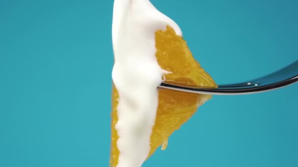 鲜奶油慢动作地在成熟的橙片上流动 在一个餐叉上的彩色蓝色背景 宏观射门 — 图库视频影像