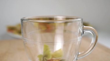 Farfalle, kelebek şeklinde pişirilmemiş makarna cam bardağa düşer. Ağır çekim. Kapat.