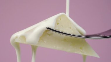 Ağır çekimde çatalın üzerine bir dilim sert peynirin üzerine krema dökmek. Renkli pembe bir arka planda. Makro atış. Geleneksel bir yemek ve tatlı.