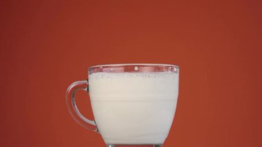 Temiz bir cam bardakta taze süt köpüğü patlatmak. Parlak bir terracotta arka planına karşı ağır çekimde.