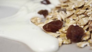 Süt, kuru üzümlü yulaf ezmesinin içine dökülür. Ağır çekim. Makro. Sağlıklı kahvaltı.