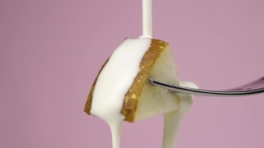 Krema olgun bir armut diliminde tatlı çatalında ağır çekimde akar. Renkli pembe bir arka planda. Makro atış. Meyve vitamini yoğurt kavramı