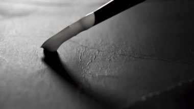 Siyah, eski, buruşuk yüzeye beyaz boya sürülmüş fırça darbesi. Koyu kağıda boya fırçası çiziyorum. Makro atış. Sanat konsepti