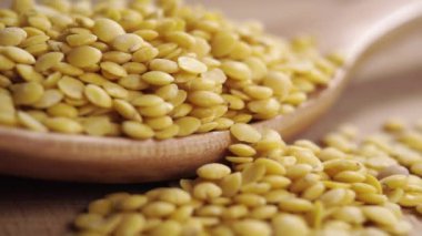 Dolu bir tahta kaşık dolusu sarı çiğ mercimek. Asyalı baklagillerin yavaş çekimde düşüp dökülmesi. Makro çekim