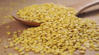 Ahşap bir yüzey üzerinde ahşap bir kaşığa pişmemiş sarı mercimeği yavaş çekimde düşmek. Kapat.