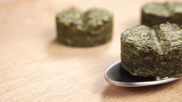 乾燥させた緑茶は 木製の表面にスプーンで錠剤の形で葉を押します マクロだ ドリーは撃たれた 自然サプリメントの概念 スーパーフードのアイデア — ストック動画