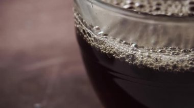 İçinde köpükler ve buhar olan cam bir fincana siyah çay dökme girdabı. Makro. Yavaş çekim