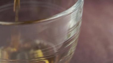 Ağır çekimde camlı fincana koyu siyah çay dökmek. Makro. Karanlık odunsu bir yüzeyde. Buharlı sabah içkisi