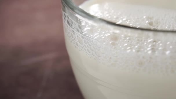 新鮮なファームミルクのフルグラスカップ 乳製品の滴下 泡が出てる 暗い木製の表面に マクロだ スローモーション — ストック動画