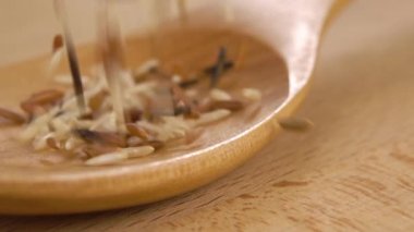 Karışık Asya çiğ pirinci ağır çekimde tahta kaşığa düşer. Makro. Basmati integrali, kırmızı ve vahşi. Kesme tahtasının üzerinde