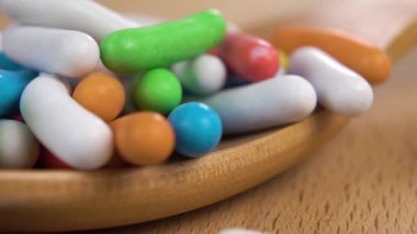 Çok renkli Dragee şekerler yavaş çekimde tahta kaşığa düşer. Parlak jöleli renkli bir doğum günü tatlısı. Makro