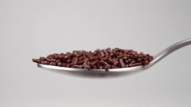 A tiny chocolate sprinkle falls in a heap in a metal dessert spoon in slow motion. Macro shot