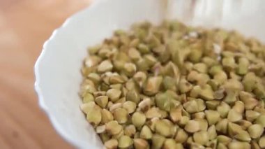 Çiğ karabuğday taneleri tahta bir yüzeyde beyaz bir kaseye düşer. Makro. Yavaş çekim