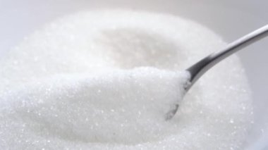 Bir kaşık dolusu şeker. Yavaş çekimde düşen beyaz kristaller. Makro çekim