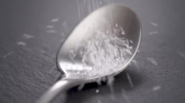 Bir çay kaşığı şekeri koyu bir mutfak yüzeyine dökülüyor. Ağır çekim. Makro