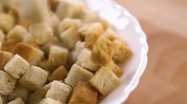 Kızarmış ekmek küpler yavaş çekimde beyaz bir kaseye düşer. Makro atış. Tahta bir yüzeyde